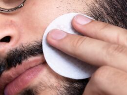 Close up image of a man washing his face and beard with a cotton pad