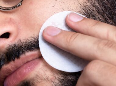 Close up image of a man washing his face and beard with a cotton pad