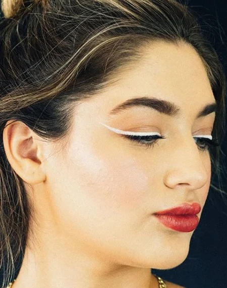 A woman looking to the side wearing minimal makeup with a long, thin white drawn out winged eyeliner. 