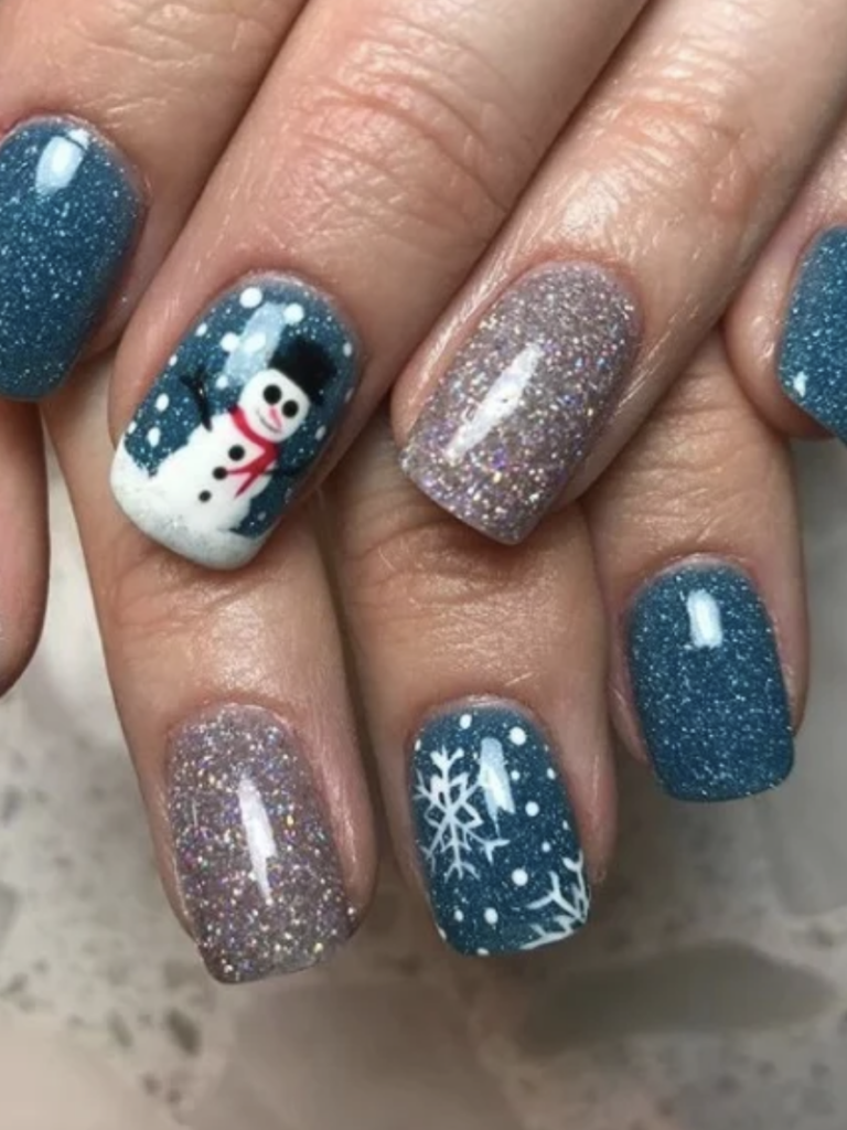 Short nails with blue and silver sparkle nail polish. One accent nail has snowflakes and the other has a snowman decal. 