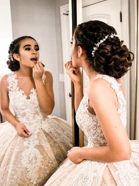 A bride touching up her lipstick in the mirror before her wedding. 