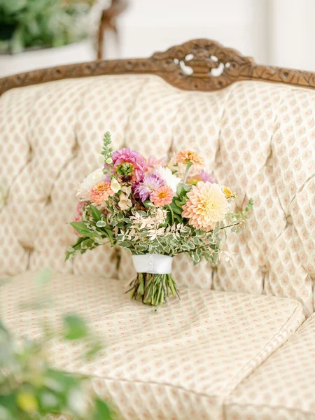 A pink, orange, and yellow wedding bouquet propped up on a couch. 