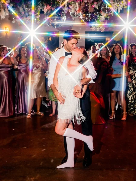 A bride and groom kissing under the bright and colorful lights on the dance floor. 