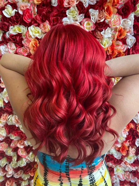 Back of a woman's head with curly bright red hair standing in front of a floral background. 