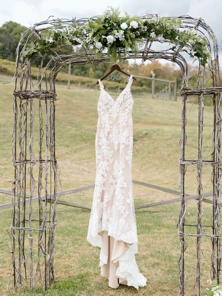 A wedding dress on a hanger hung from an arch on a green field. 