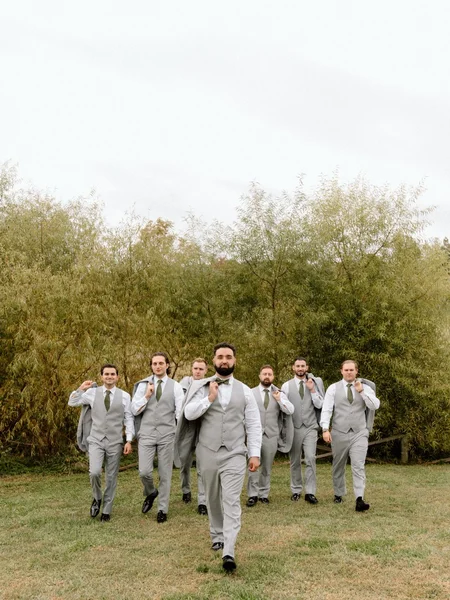 A group of groomsmen led by the groom strutting towards the camera with their jackets thrown over their shoulder. 
