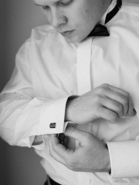 Black and white photo of a groom looking down at his sleeve as he puts on his cufflinks.