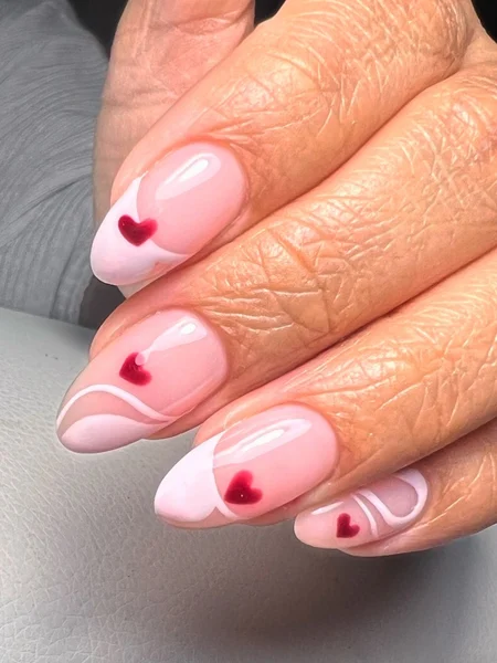 Manicure with light pink tips and red heart decals. 