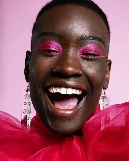 Black woman smiling and wearing hot pink eyeshadow.