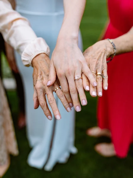 Three generations of women hold their hand out to show off their wedding rings. 