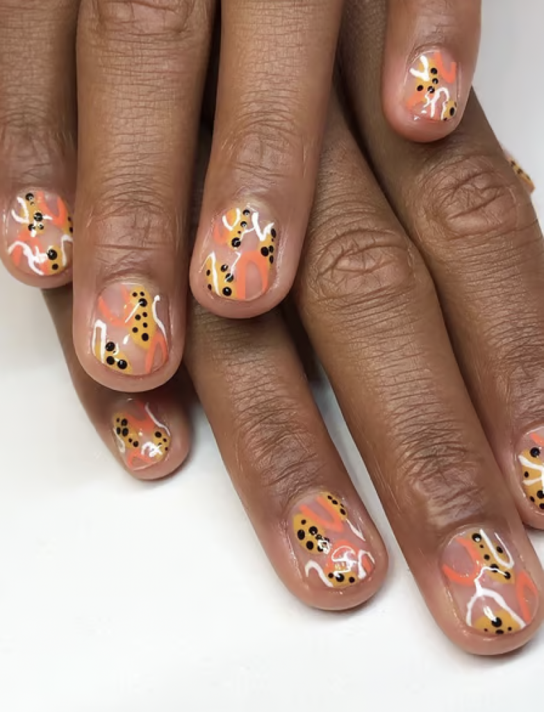 Nail design on short nails with an abstract pattern consisting of peach, yellow, white, and black dots and swirls. 