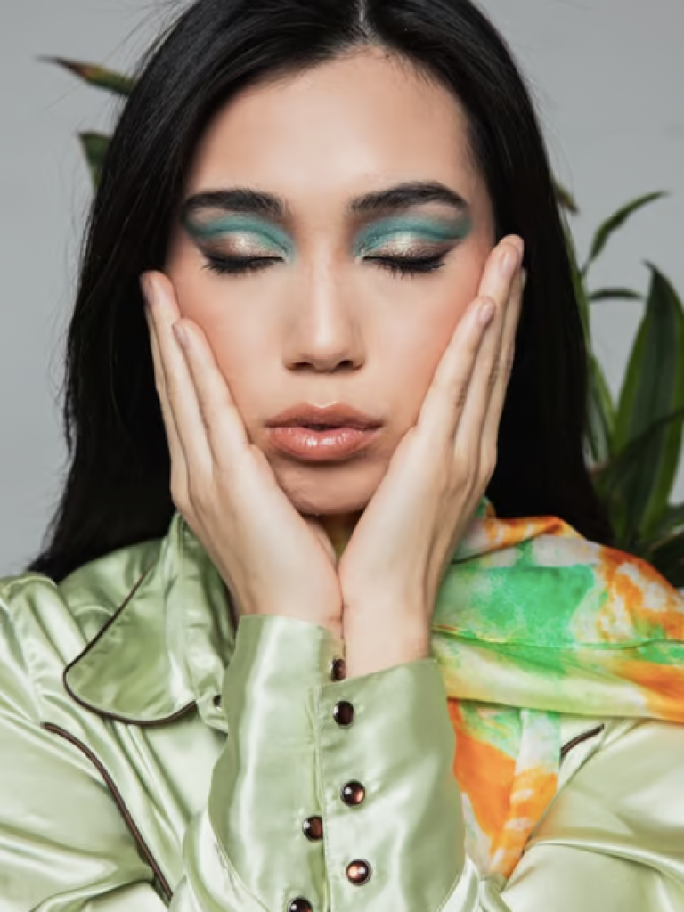 A woman with her eyes closed and an emerald green cut crease eyeshadow look. 