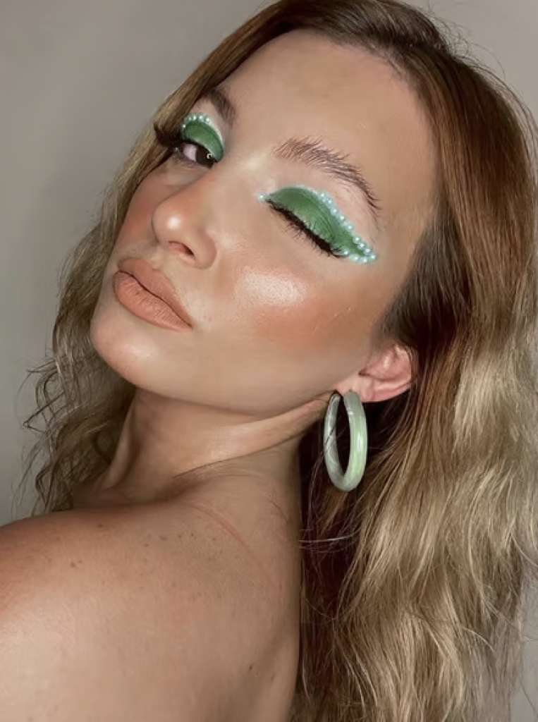 A woman with bright green, winged eyeshadow outlined with green pears. 