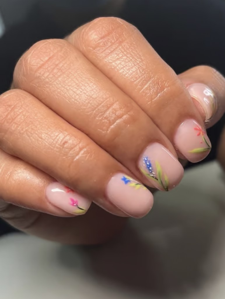 Short nails with a nude base coat and delicate floral designs painted on each nail. 