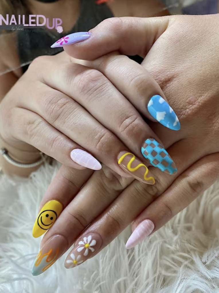 A mix & match nail design with a different pattern on each nail; Patterns include clouds, a smiley face, daisies, flames and pink and yellow swirls. 