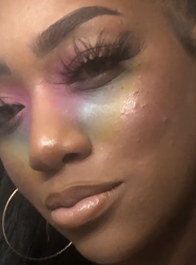 A woman wearing rainbow highlighter brushed across the cheek and eyes; Perfect for festive St. Patrick's Day glam. 