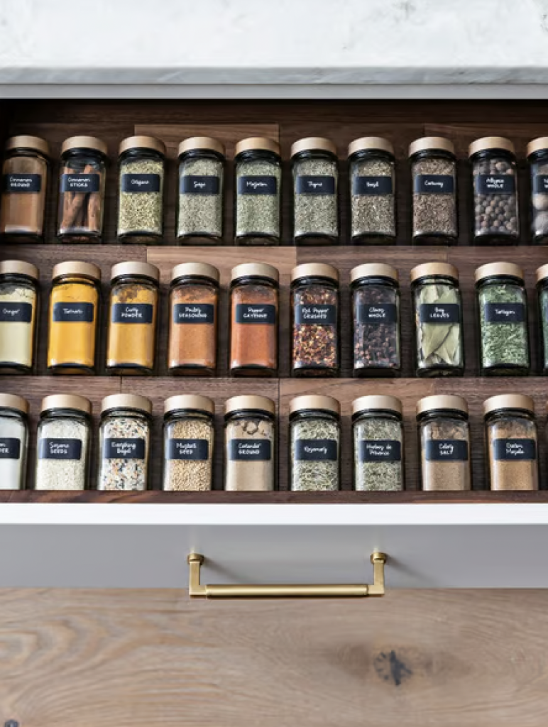 A spice drawer with all of the spices in glass containers with black labels. 