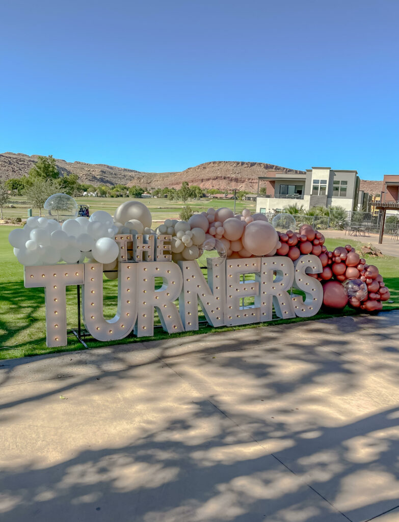 Large market light letters spelling out "The Turners" with a white, beige, and pink balloon garland surrounding it. 