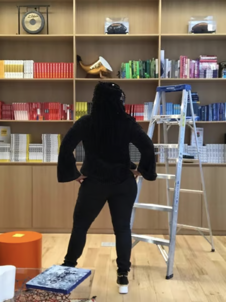 A professional organizer standing in front of bookshelves that have been organized and color coded. 