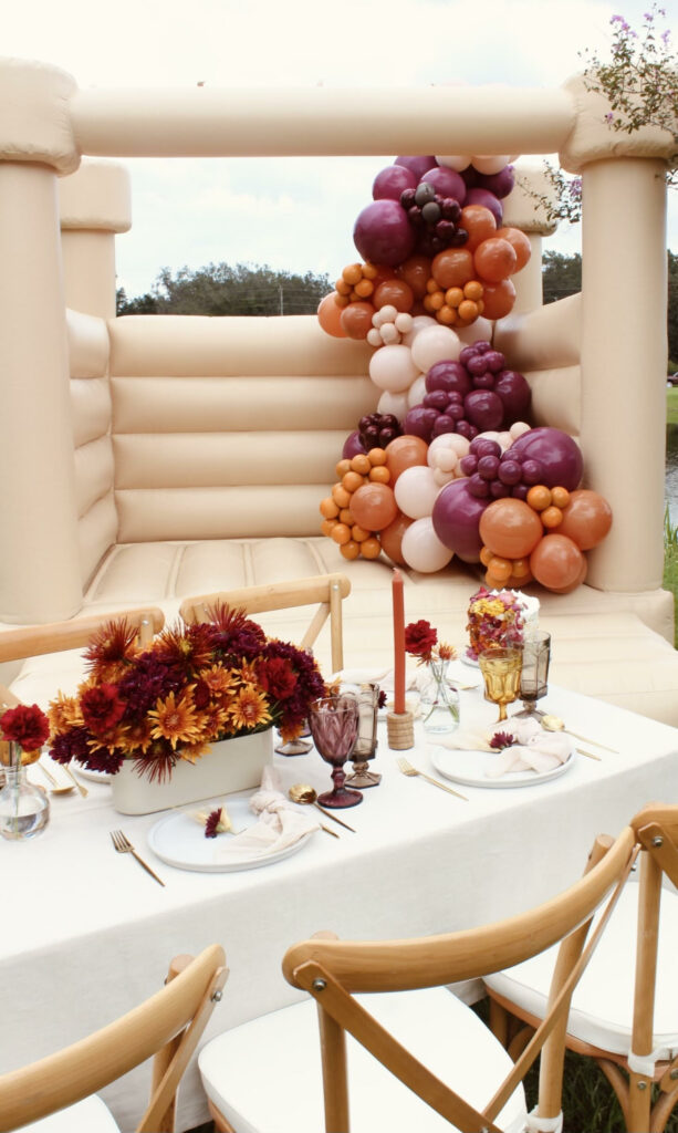 An orange, purple, and beige balloon garland inside of a neutral colored bounce house for a Friendsgiving party.