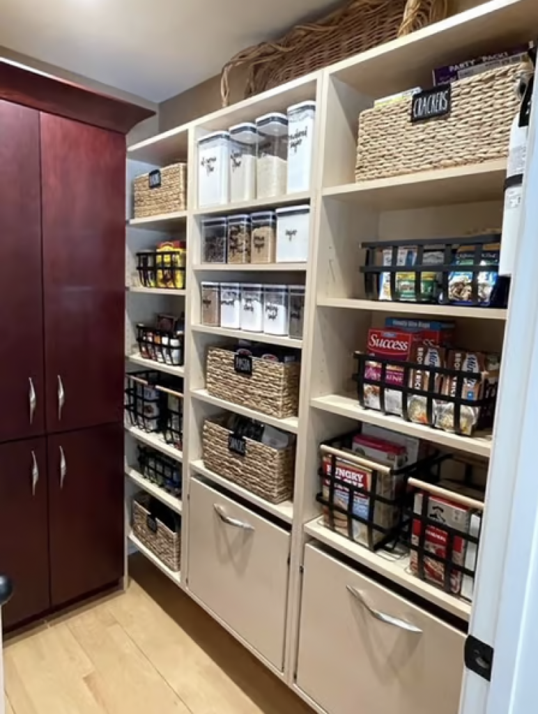 An organized pantry with woven bins and plastic food containers that have all been labeled. 
