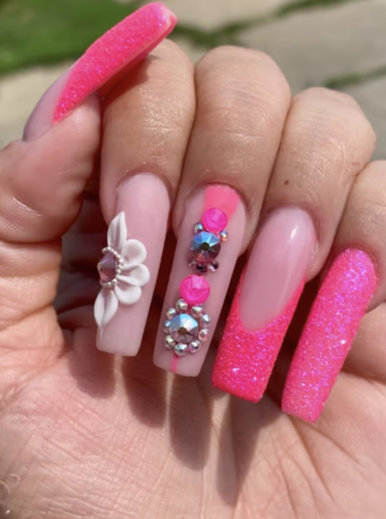 A mix of light pink and hot pink nails with rhinestone and floral decals. 
