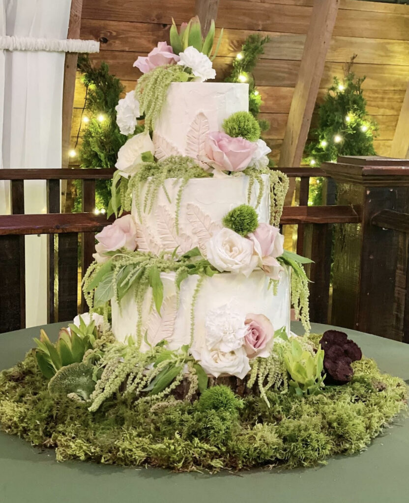 a three-tiered fairytale wedding cake with pink roses, leaves and moss. 
