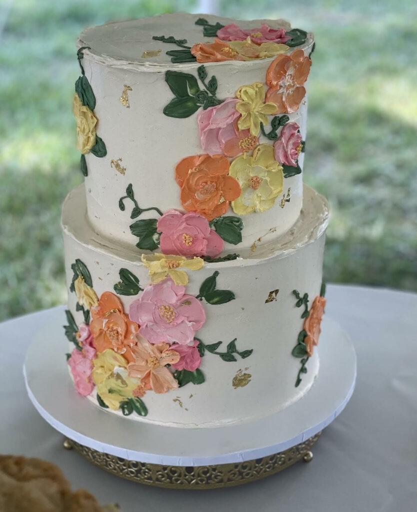 A two-tiered wedding cake with handprinted orange, yellow and pink flowers. 