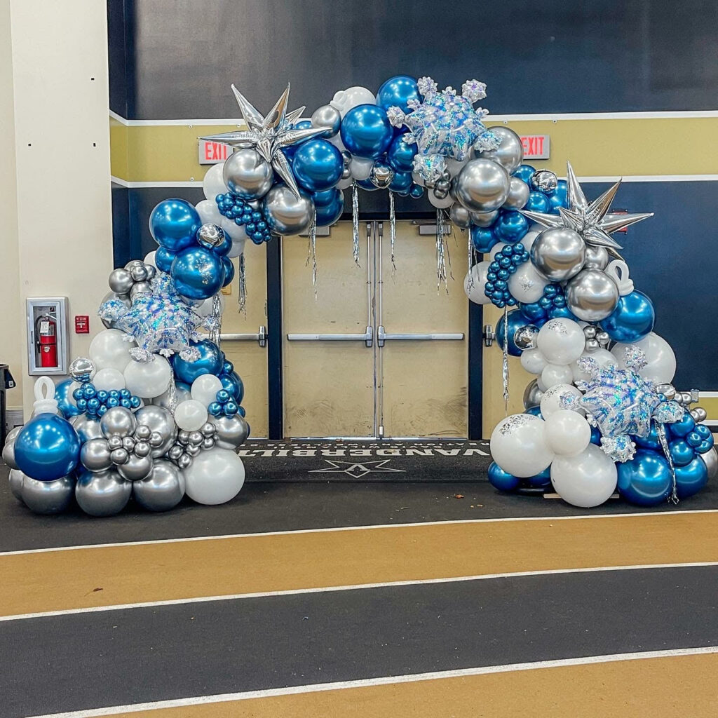 A large white, chrome blue, and chrome silver balloon arch with snowflake, starburst and ornament embellishments for a company holiday party. 