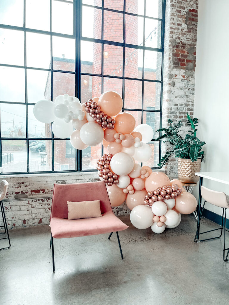 A 12ft pink, white, and chrome balloon garland around a pink chair for a baby shower. 