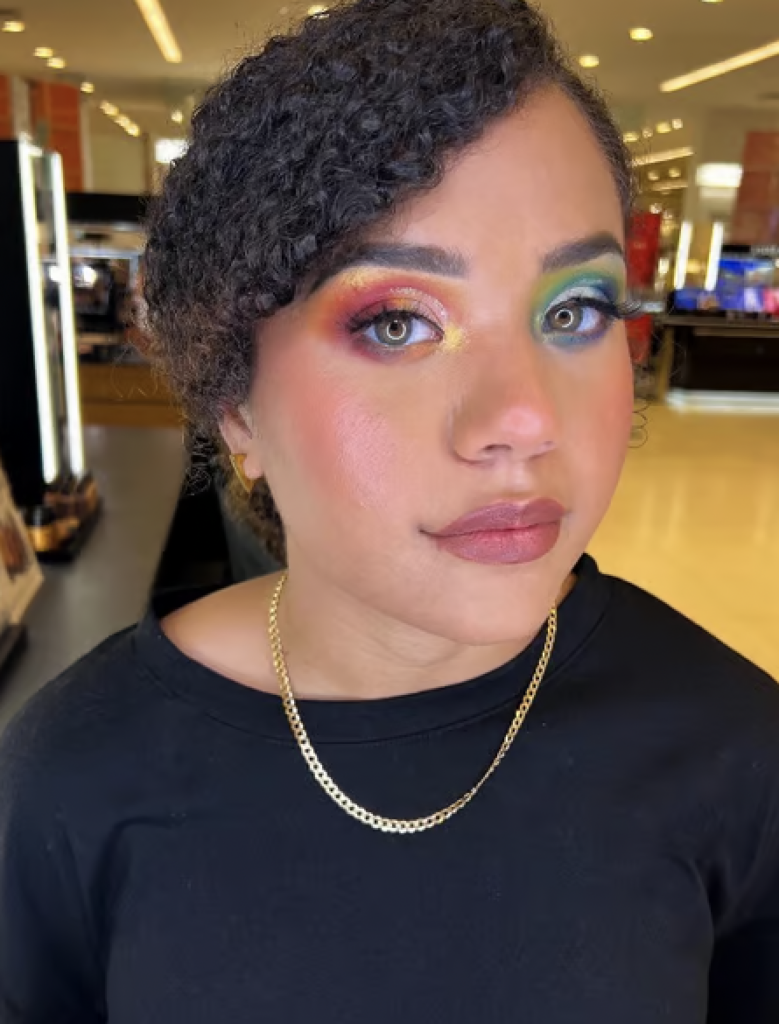 A woman with rainbow eyeshadow; One eye has the colors red orange and yellow and the other green blue and purple.