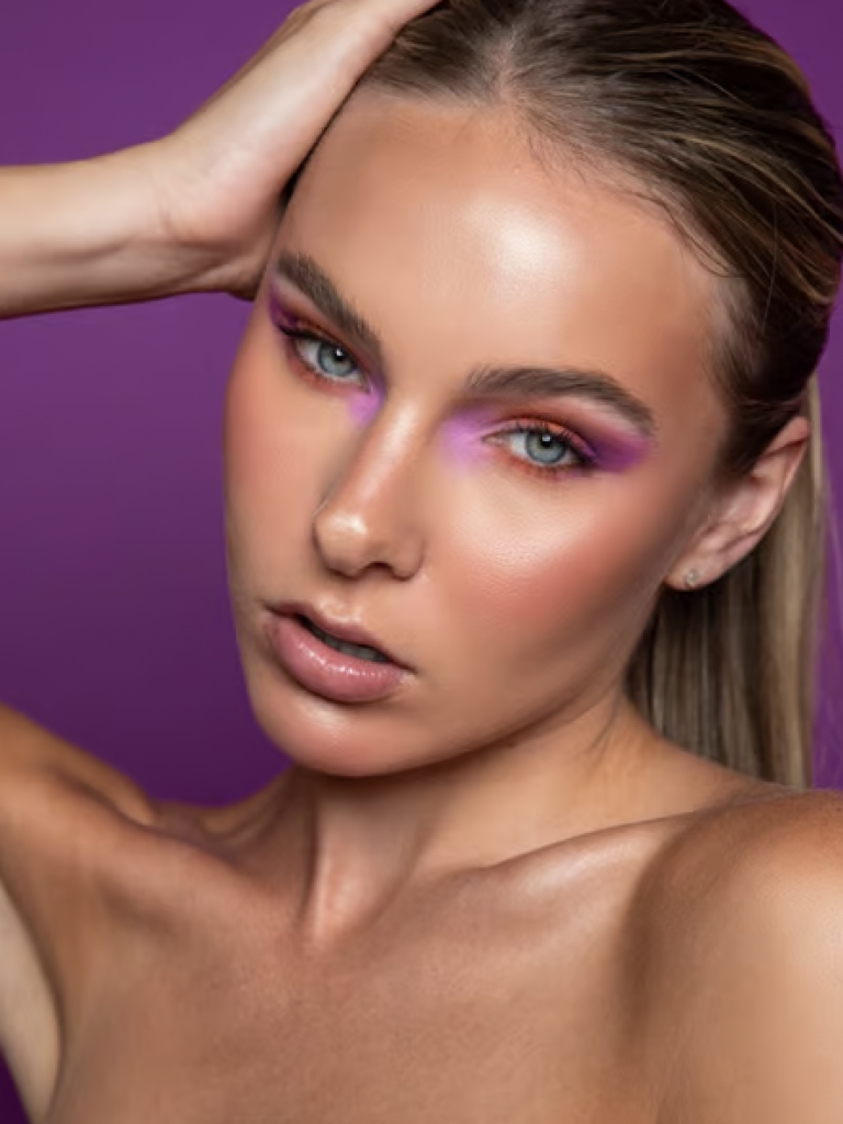 A woman with orange eyeshadow on her lids and under her eyes with hot pink eyeshadow in the inner and outer corners. 