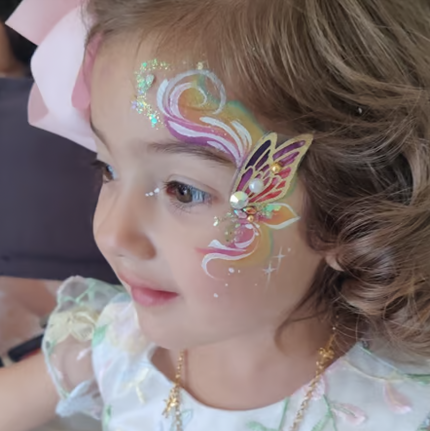 A colorful painted butterfly on the side of the face with pearl and glitter accents.