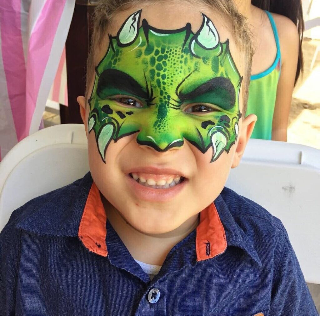 A kid with green dragon face paint with white horns and dark green scales. 