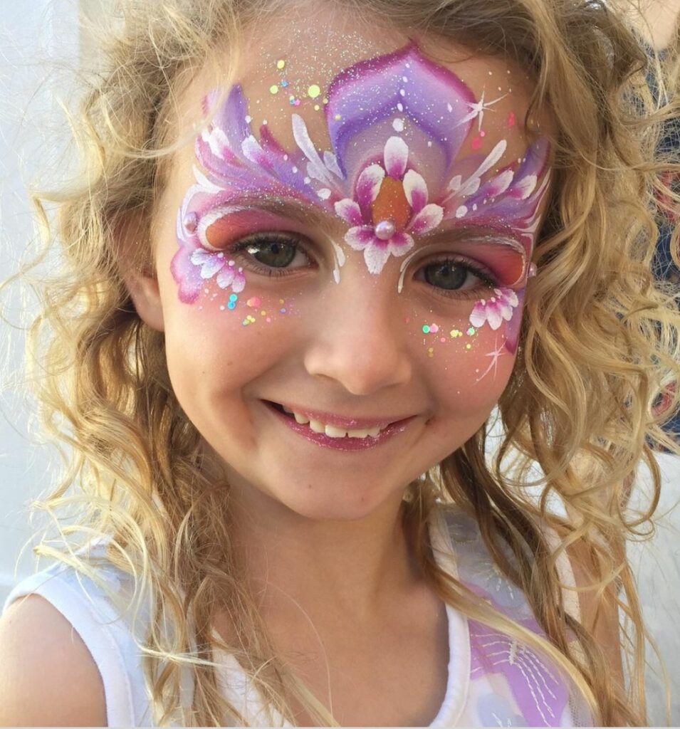 Purple, pink and white face paint in a floral, fairy-like design on the eyes and forehead. 