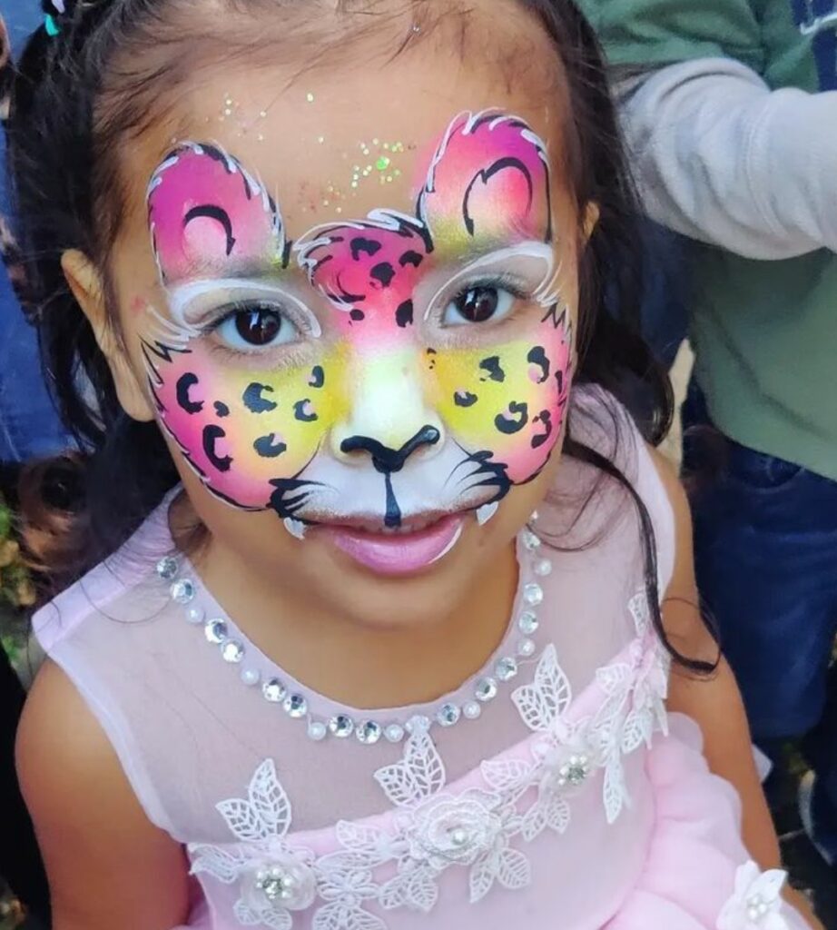 Neon pink and yellow leopard/wild cat face paint with round ears and black spots. 