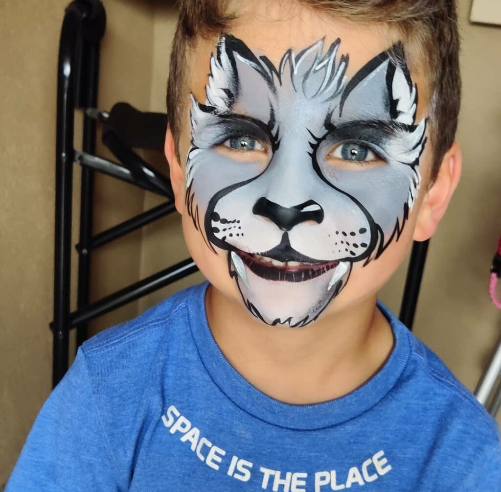 A little boy with a cartoon wolf painted on his face. 