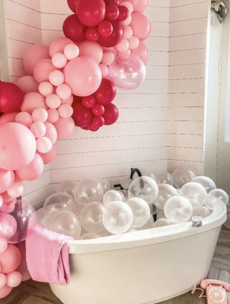 Clear balloons in a bathtub to look like a bubble bath with a balloon garland in different shades of pink surrounding the tub. 