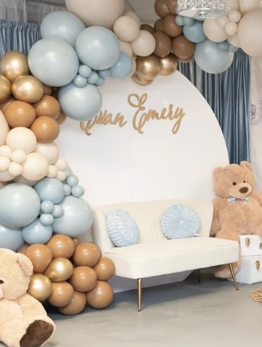 Blue, gold and white balloons surrounding a backdrop and couch for a bear themed baby shower. 
