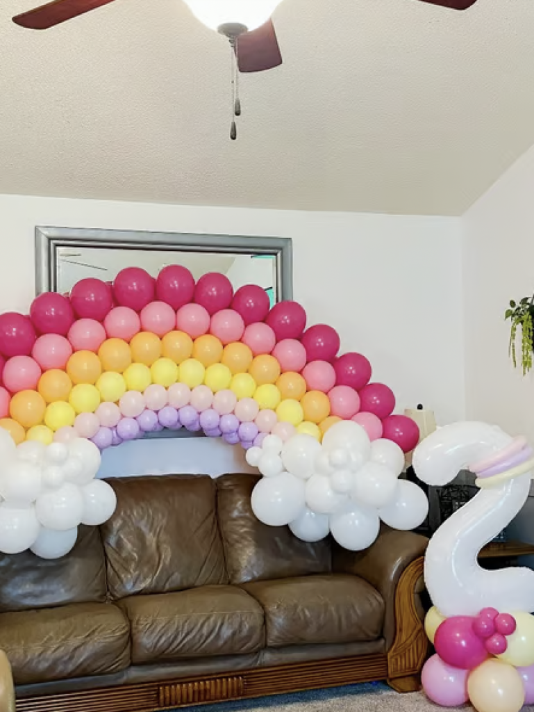 Balloon arch shaped like a rainbow with 2 clouds draped over a couch for a 2-year-old's birthday party. 