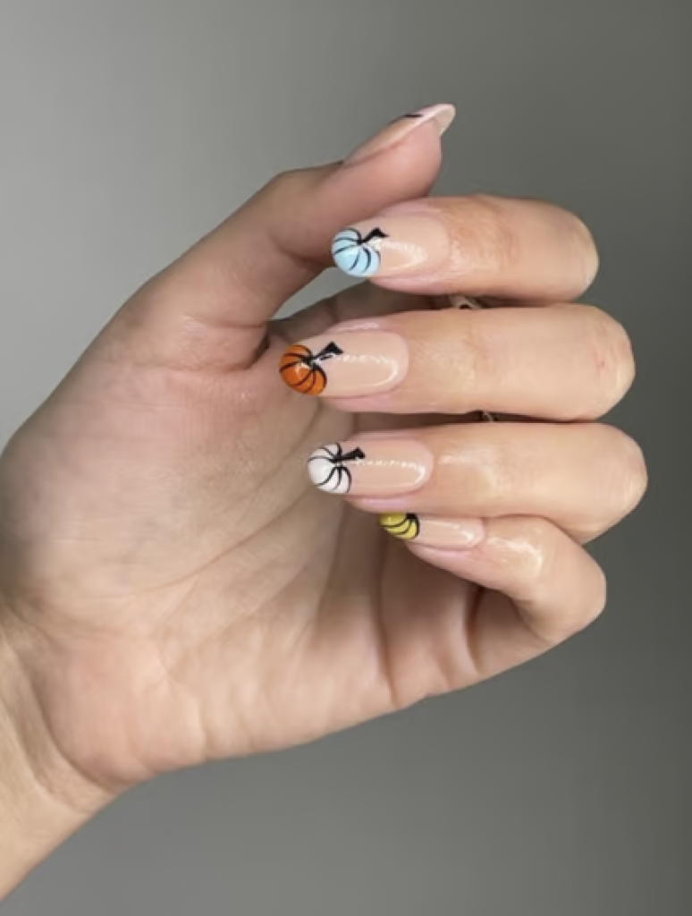 Neutral colored manicure with different color pumpkins on each nail tip. 