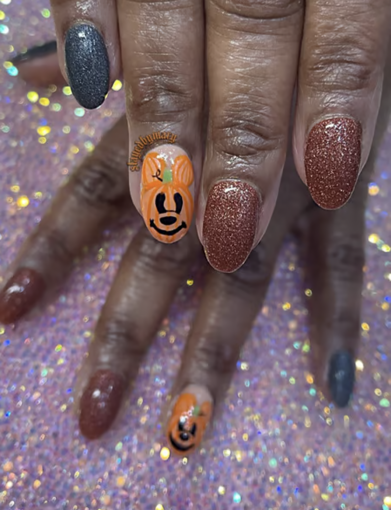 Black and orange glitter nails with a ring finger decal of a pumpkin mickey mouse. 