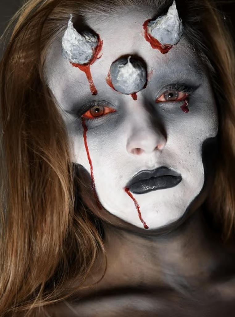 Devil Makeup with three horns, grey face makeup, and bloody eyes